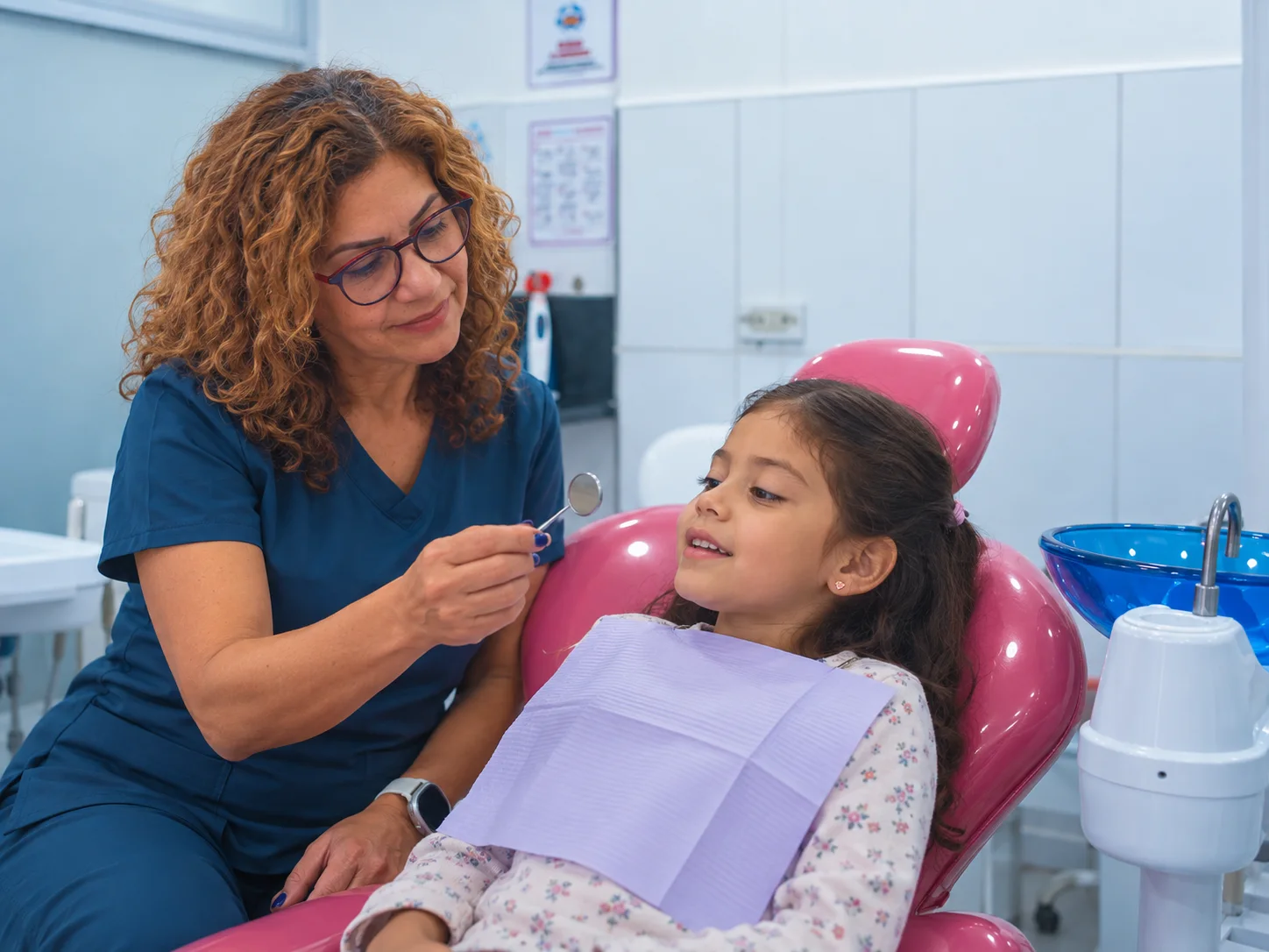 Odontóloga muestra un espejo dental a una niña en el sillón rosado del consultorio